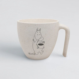 Puu- ja sokeriruokopohjaisista raaka-aineista valmistettu orgaaninen vaalea kuppi, jossa pitkä pöytää asti ulottuva kahva ja kyljessä Muumipeikko, joka soittaa kaulassaan roikkuvaa kattilaa kuin rumpua.