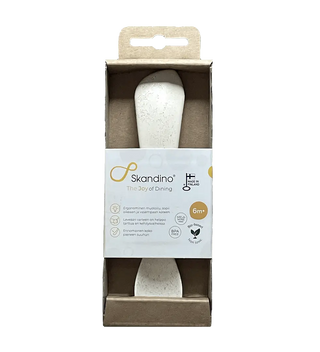 A white baby spoon in eco-friendly "Product Packaging (Spoon)" labeled "Skandino, The Joy of Dining," for ages 6+ months, with icons indicating it's BPA-free and made from 100% plant-based materials.