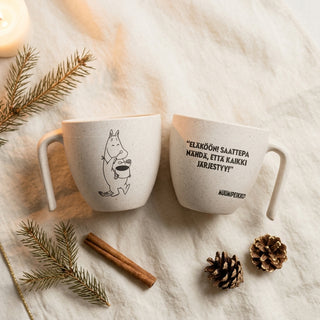 Muumipeikko Muumimuki pöydällä, mukin molemmat puolet näkyy ja teksti on: "Eläköön! Saattepa nähdä, että kaikki järjestyy!"